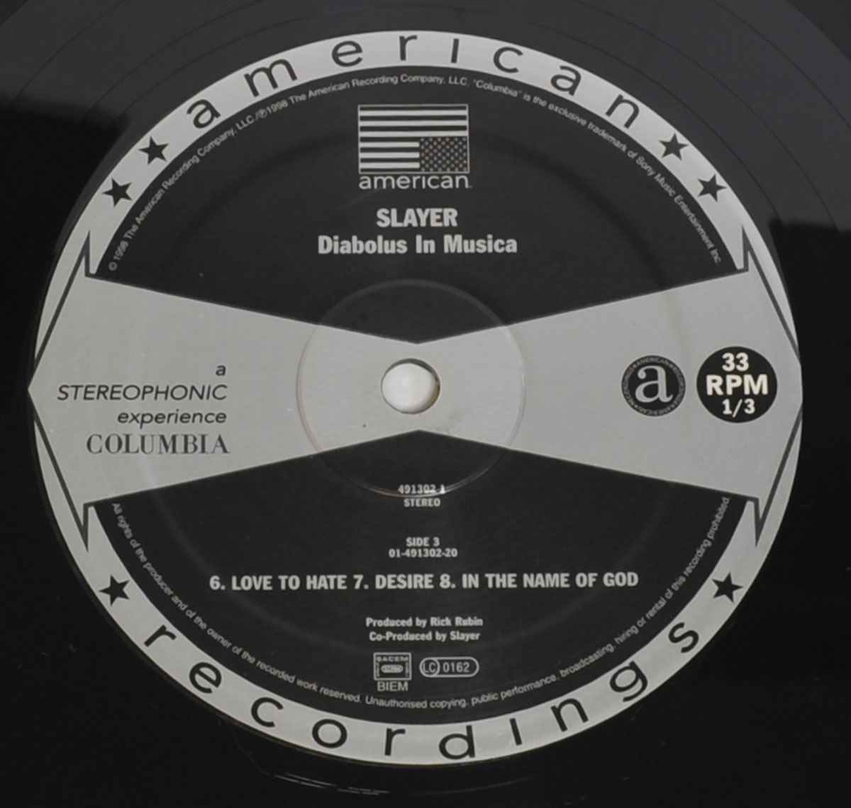 Close-up of Slayer's 'Diabolus in Musica' vinyl record label, featuring American Recordings and Columbia logos, tracklist, and production details on a black-and-white design.